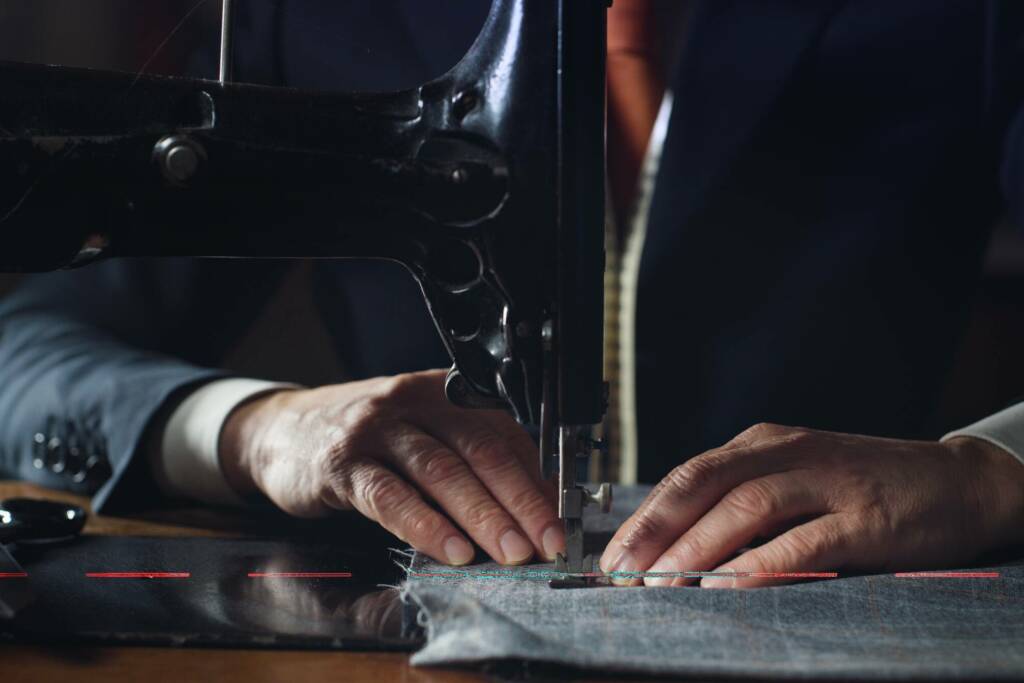 Close up shot of experienced tailor is sewing custom handmade high quality apparel in ancient luxury traditional tailoring workshop. Concept of industry, handmade, hand craft, couturier and tradition.