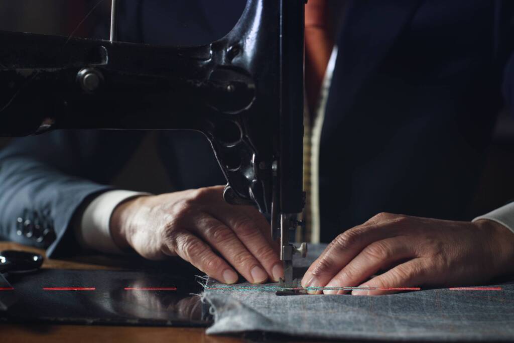 Close up shot of experienced tailor is sewing custom handmade high quality apparel in ancient luxury traditional tailoring workshop. Concept of industry, handmade, hand craft, couturier and tradition.